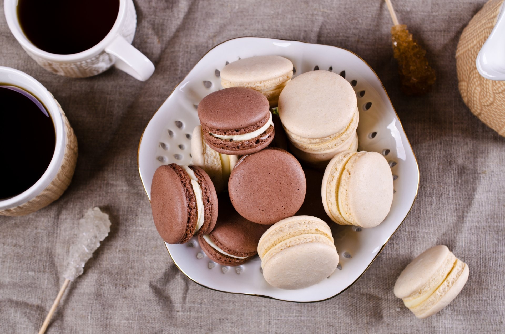 A 4K Ultra HD desktop wallpaper featuring a plate of assorted macarons alongside cups of coffee on a textured fabric surface, highlighting sweets and food themes.