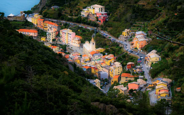 Colorful Ligurian village of pastel houses and a central church, nestled in terraced green hills by the sea — 4K Ultra HD PC desktop wallpaper of a man-made hillside settlement.