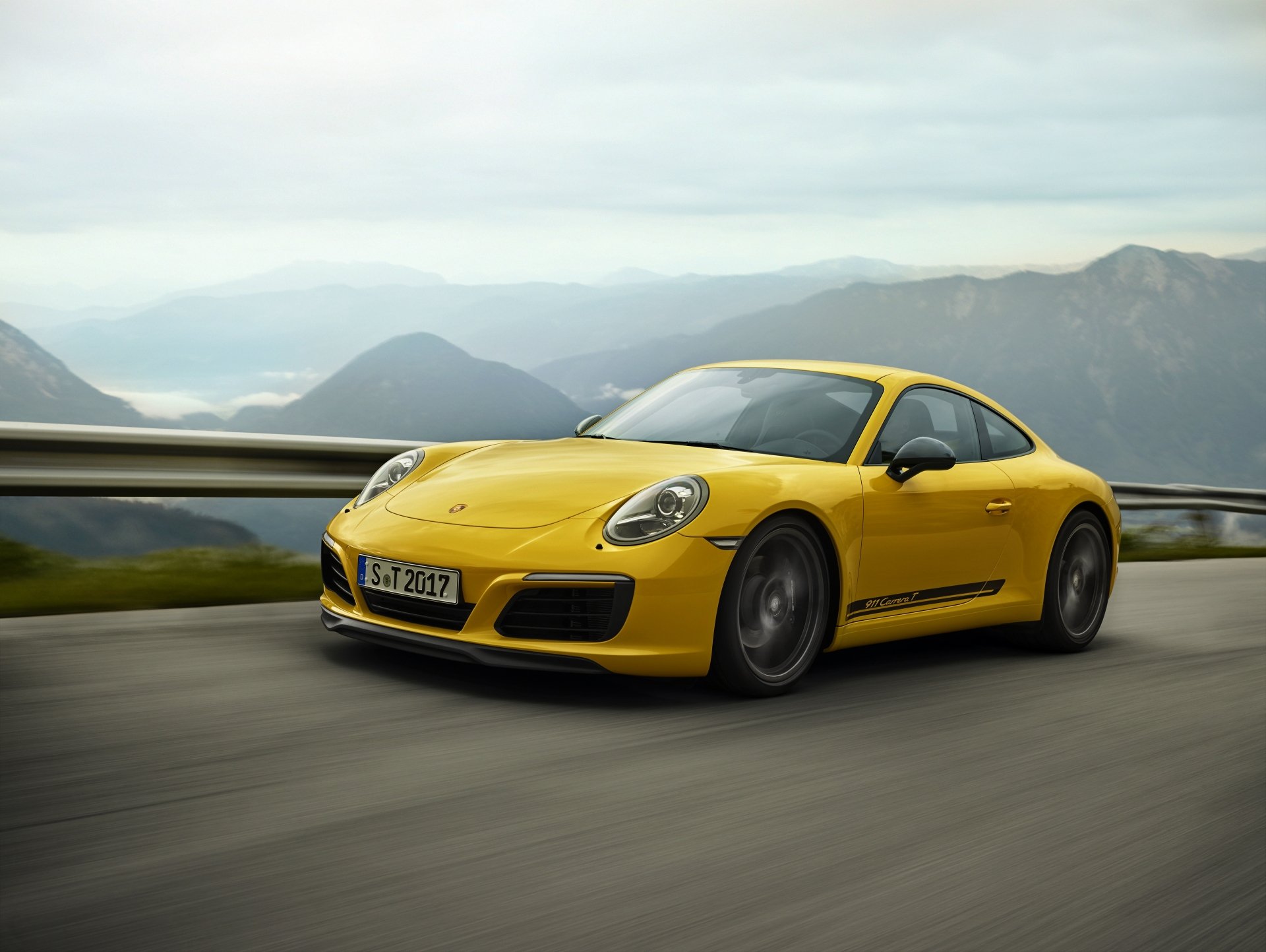 Yellow Porsche 911 Carrera T sports car driving on a mountainous road, captured in 4K Ultra HD for a dynamic PC desktop wallpaper.