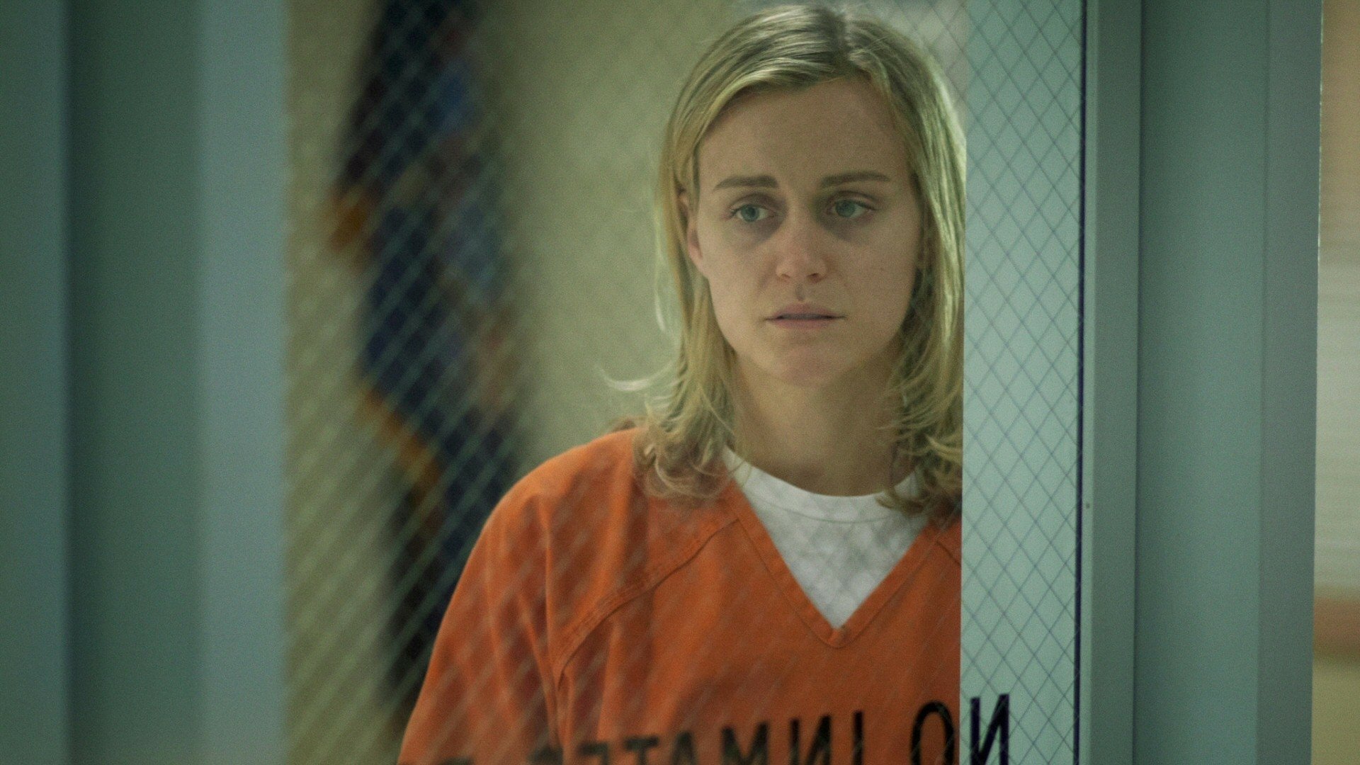HD PC desktop wallpaper/background from the TV show Orange Is the New Black: woman in an orange prison uniform behind wired glass, looking solemn.