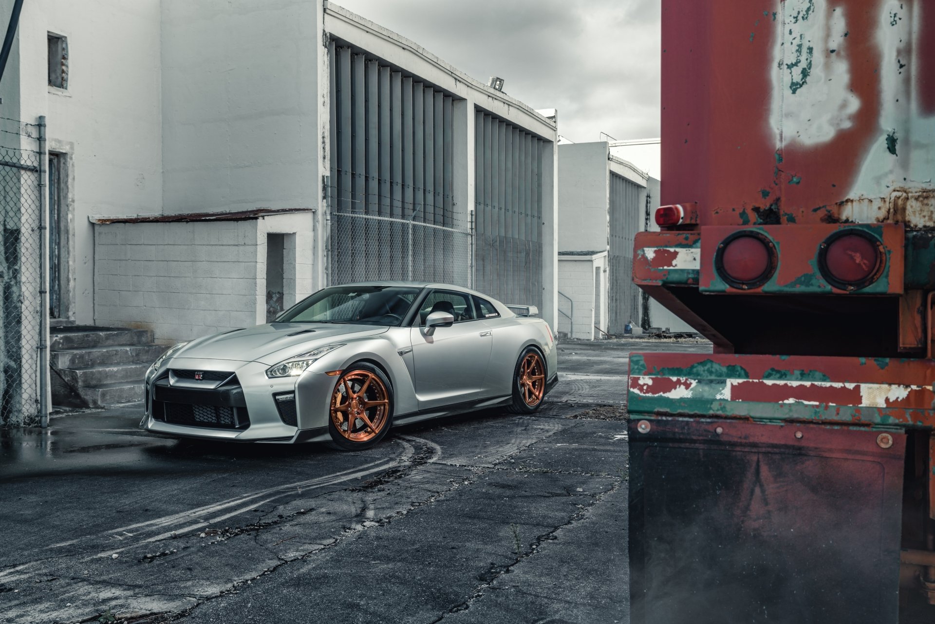 Silver Nissan GT-R supercar with orange rims parked in an urban industrial setting, captured in stunning 8K Ultra HD as a PC desktop wallpaper and background.