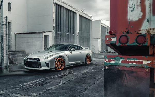 Silver Nissan GT-R supercar with orange rims parked in an urban industrial setting, captured in stunning 8K Ultra HD as a PC desktop wallpaper and background.