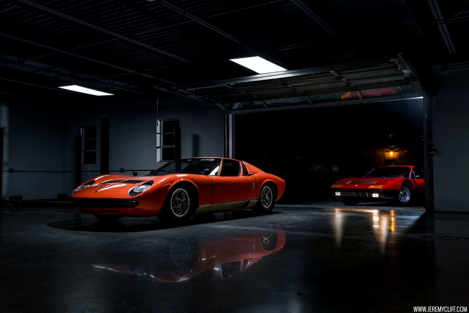 Orange Lamborghini Miura in a dim garage with glossy floor reflections, a second Miura in the background — HD PC desktop wallpaper of a classic car/vehicle.