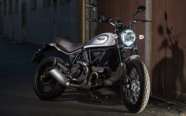 Ducati Scrambler motorcycle parked against a dim urban wall, high-detail 4K Ultra HD PC desktop wallpaper showing the bike's chrome headlight, brown leather seat and rugged tires.