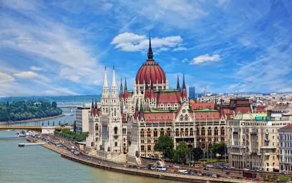 HD wallpaper of the cityscape in Budapest, Hungary, featuring a majestic bridge over a river and grand architecture, highlighting a beautiful building with a red dome under a bright blue sky.