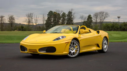 Yellow Ferrari F430 convertible parked on asphalt with trees and hills in the background, captured in a crisp 4K Ultra HD desktop wallpaper.