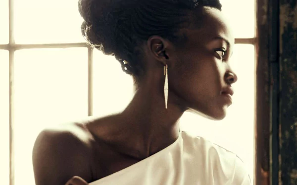 HD PC desktop wallpaper: profile portrait of a celebrity woman with braided updo and gold earring, wearing a white one-shoulder top, bathed in soft window light and warm tones.