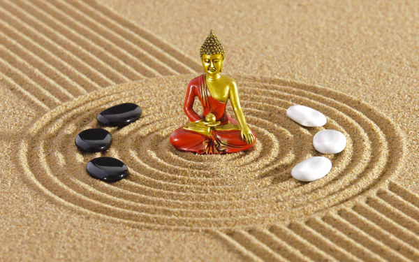 HD desktop wallpaper featuring a golden and red Buddha statue surrounded by black and white stones on raked sand, evoking a sense of zen and tranquility.