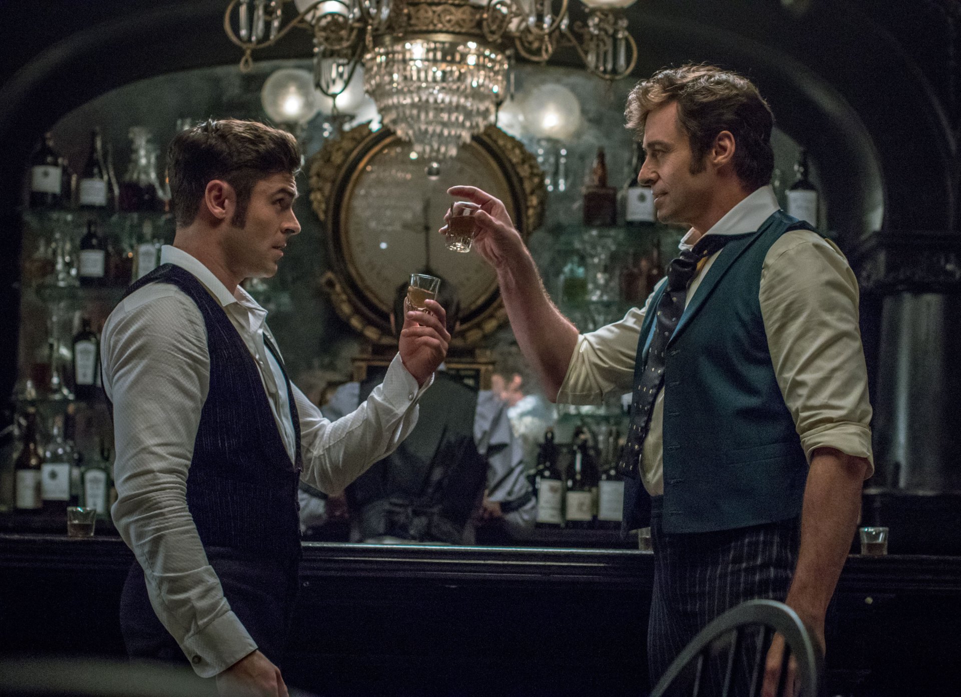 HD desktop wallpaper from The Greatest Showman featuring two characters toasting glasses in a dimly lit bar.