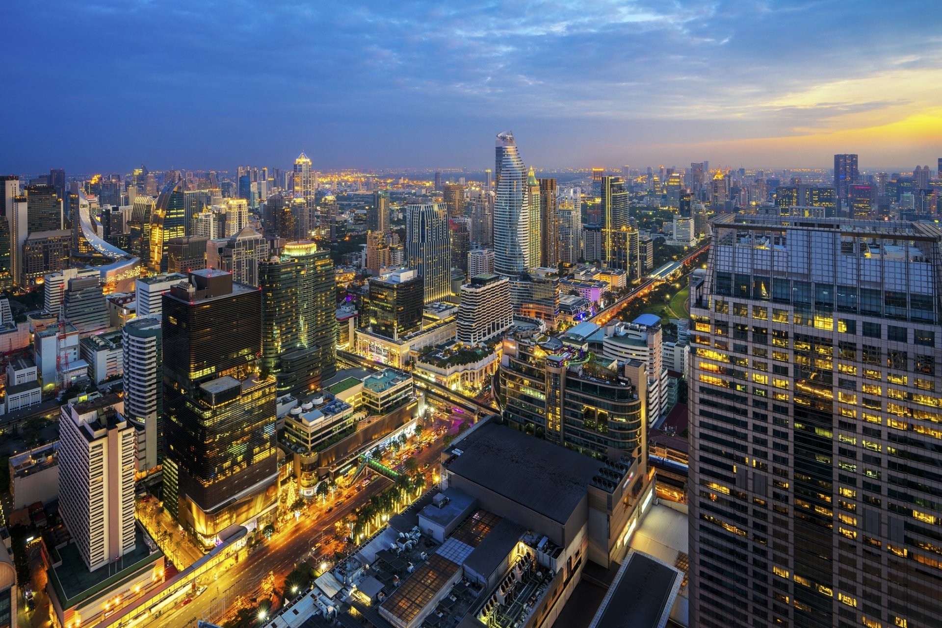 A vibrant view of Bangkok’s cityscape at dusk, featuring illuminated skyscrapers and busy streets in this HD desktop wallpaper showcasing Thailand’s urban skyline.