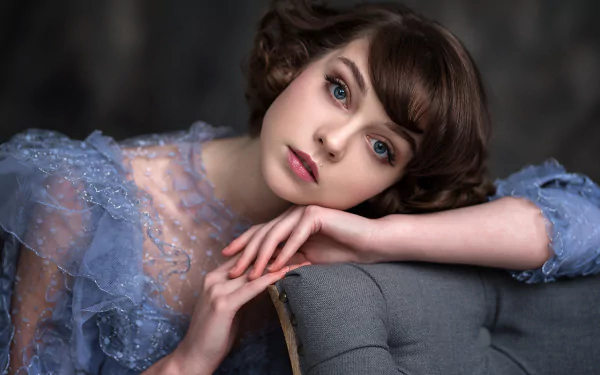HD desktop wallpaper featuring model Olya Pushkina with short brunette hair, striking blue eyes, and subtle lipstick, wearing a delicate lace dress.