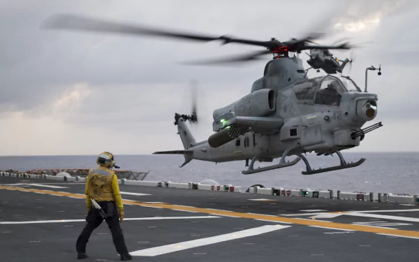 HD desktop wallpaper featuring a Bell AH-1Z Viper military attack helicopter hovering over a ship deck with a crew member nearby.