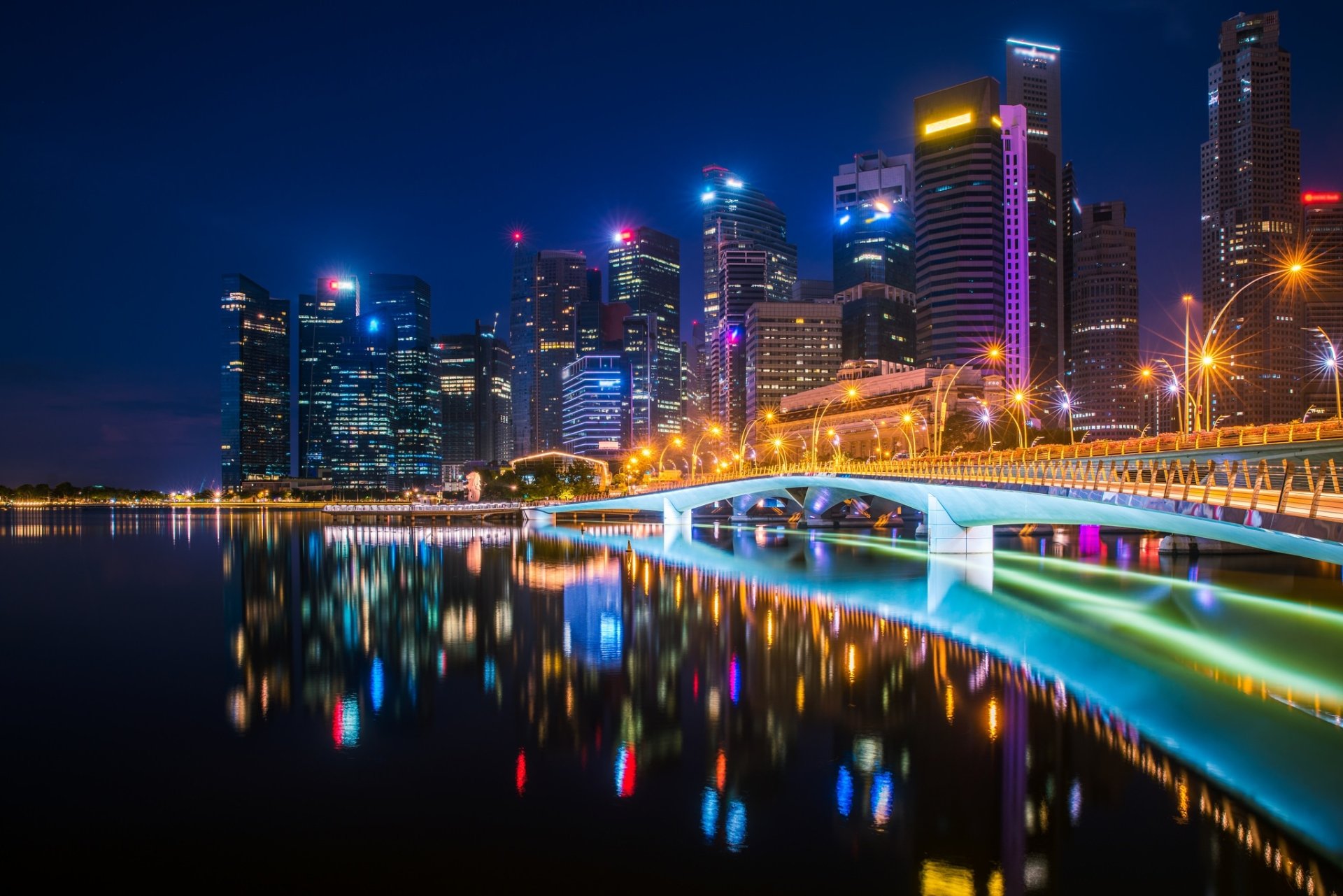 Night view of Esplanade Bridge in Singapore, with illuminated skyscrapers reflecting on the water. This HD desktop wallpaper highlights the city's vibrant nightlife and modern architectural beauty.