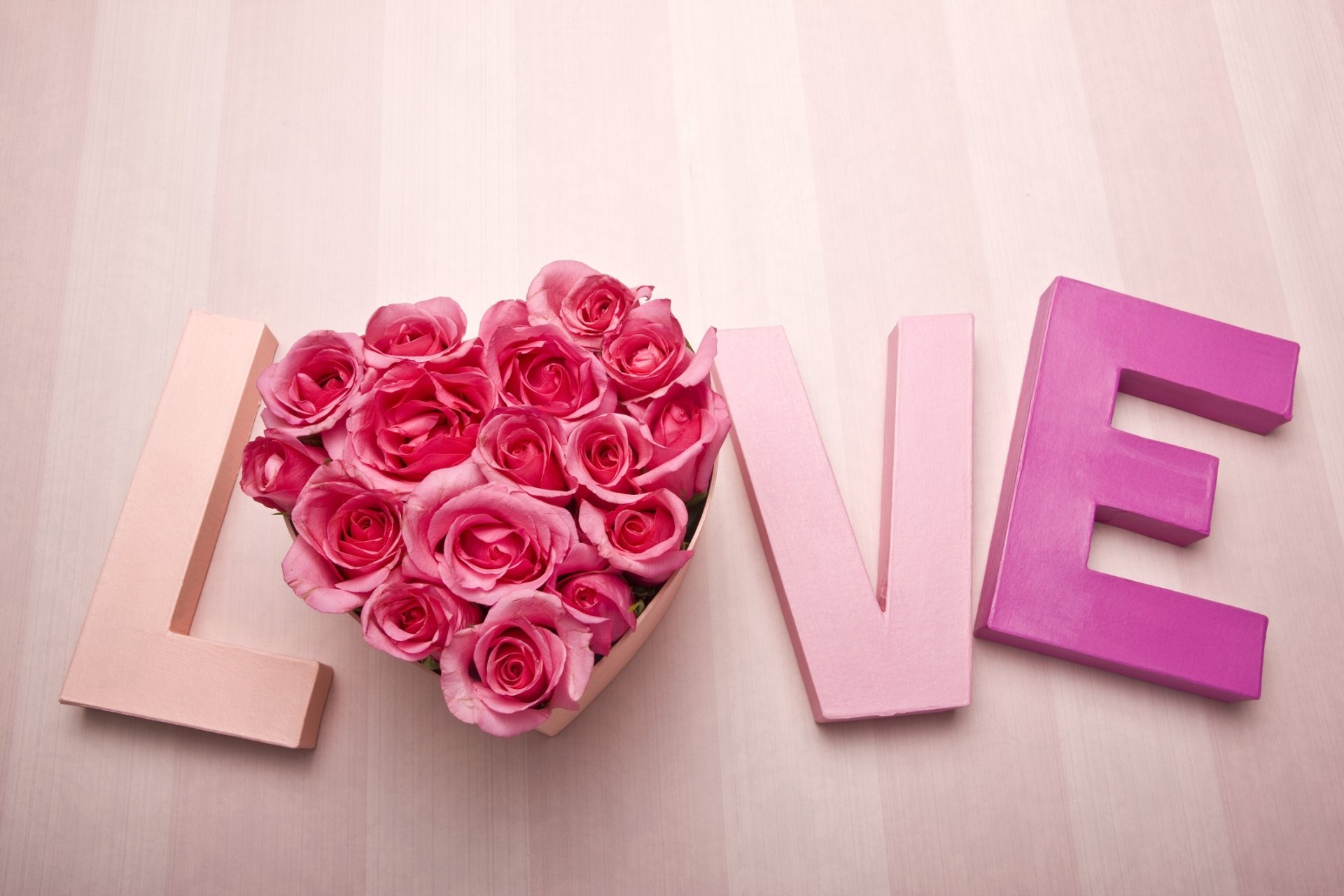 HD desktop wallpaper with the word LOVE spelled out, featuring a heart-shaped arrangement of pink roses in place of the O. Background is a light pink, enhancing the romantic and loving atmosphere.