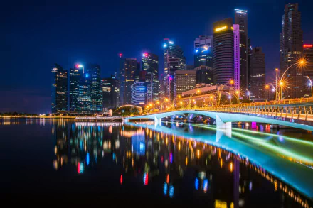 Night view of Esplanade Bridge in Singapore, with illuminated skyscrapers reflecting on the water. This HD desktop wallpaper highlights the city's vibrant nightlife and modern architectural beauty.