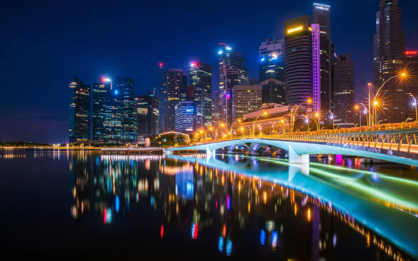 Night view of Esplanade Bridge in Singapore, with illuminated skyscrapers reflecting on the water. This HD desktop wallpaper highlights the city's vibrant nightlife and modern architectural beauty.