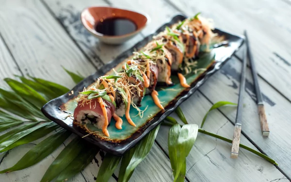 HD desktop wallpaper featuring a still life of sushi rolls with fish, rice, and sauce, accompanied by chopsticks and a dish of soy sauce on a rustic wooden surface.