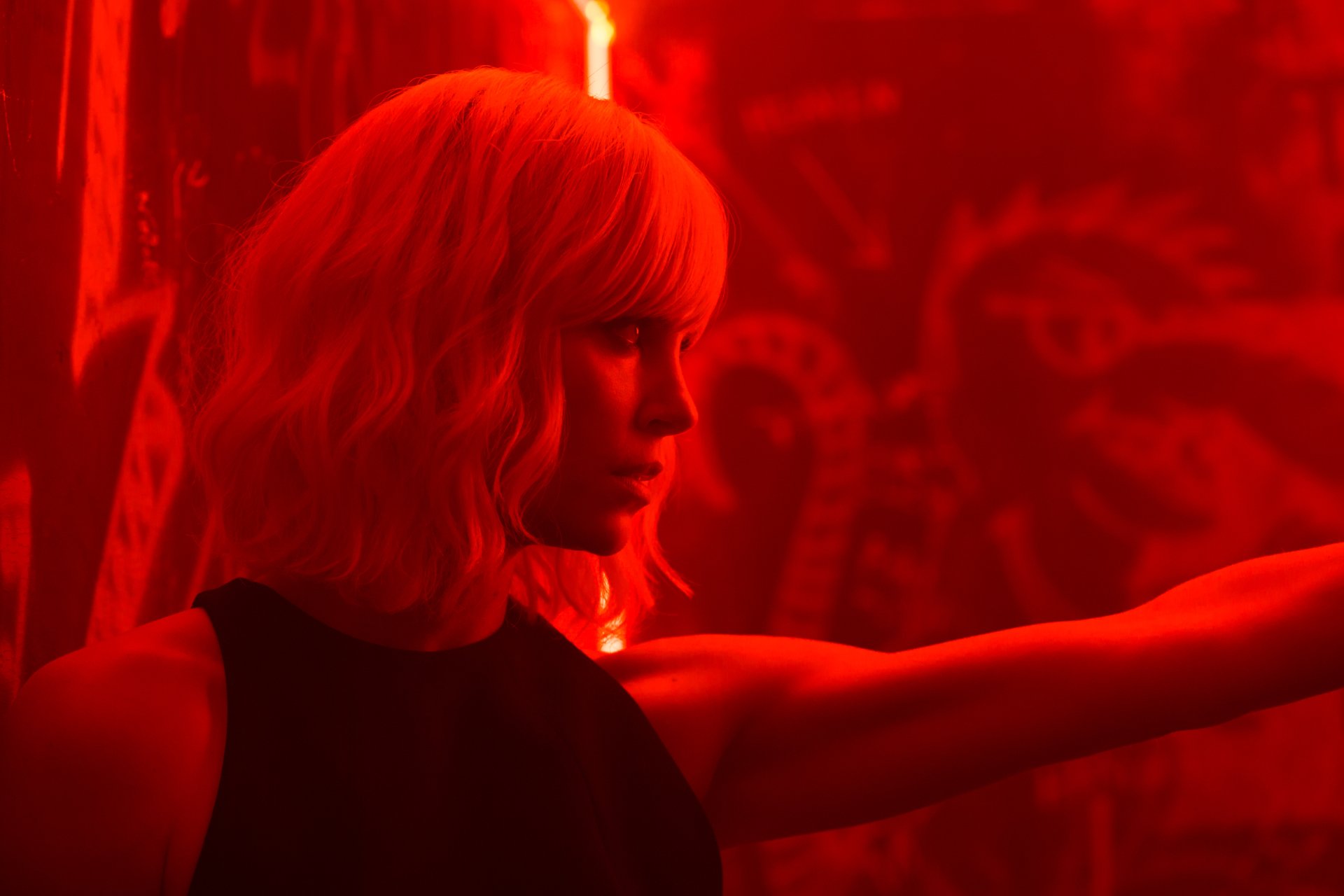 HD desktop wallpaper featuring Charlize Theron as the lead character in the movie Atomic Blonde, bathed in red lighting with a focused, intense expression.