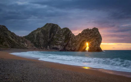 Sunrise over Durdle Door arch on a beach, with clouds above the ocean horizon, captured in stunning HD for a PC desktop wallpaper background.