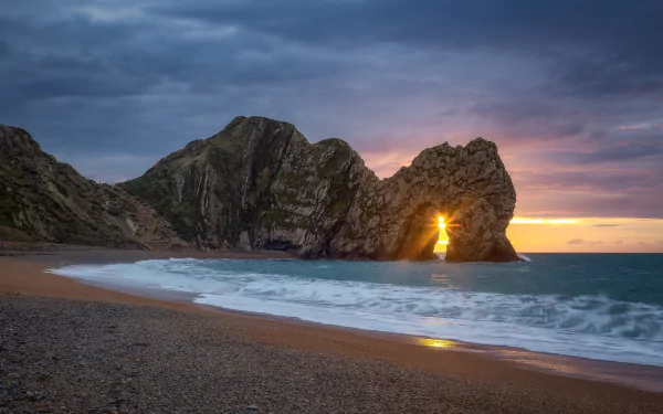 Sunrise over Durdle Door arch on a beach, with clouds above the ocean horizon, captured in stunning HD for a PC desktop wallpaper background.