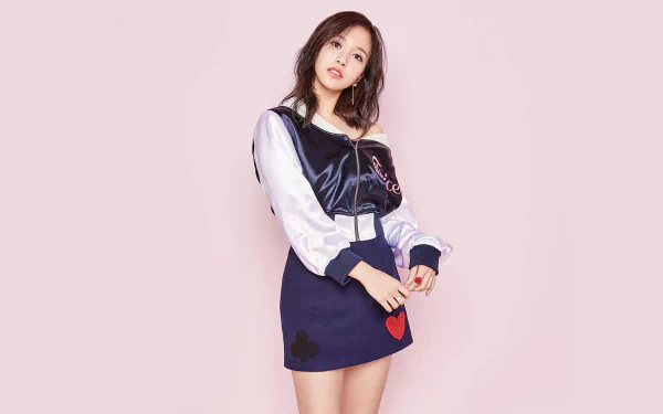HD desktop wallpaper featuring Mina from K-pop group TWICE, wearing a skirt, with long black hair and brown eyes, set against a soft pink background.