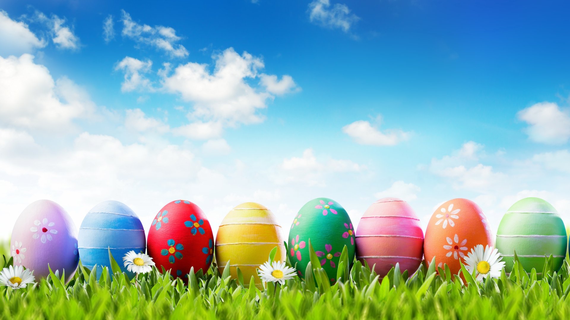 Vibrant Easter eggs in various colors rest on green grass under a bright blue sky with fluffy clouds, captured in stunning 8K Ultra HD for a festive holiday backdrop.