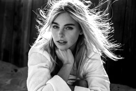 Black-and-white HD desktop portrait of a smiling female model with long windblown hair and freckles, posed casually against a dark monochrome background.