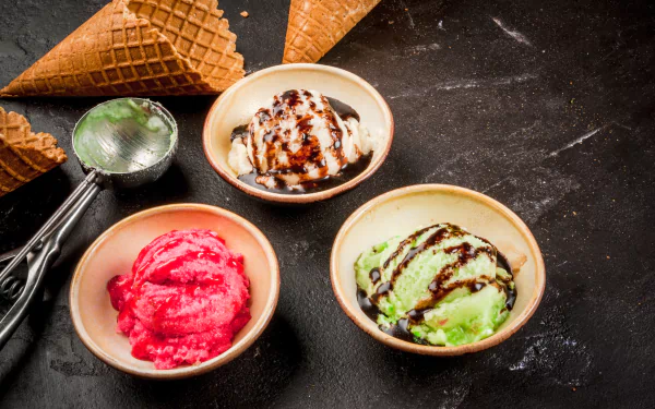 4K Ultra HD PC desktop wallpaper still life of three colorful ice cream scoops in bowls with waffle cones and a metal scoop on a dark textured background.
