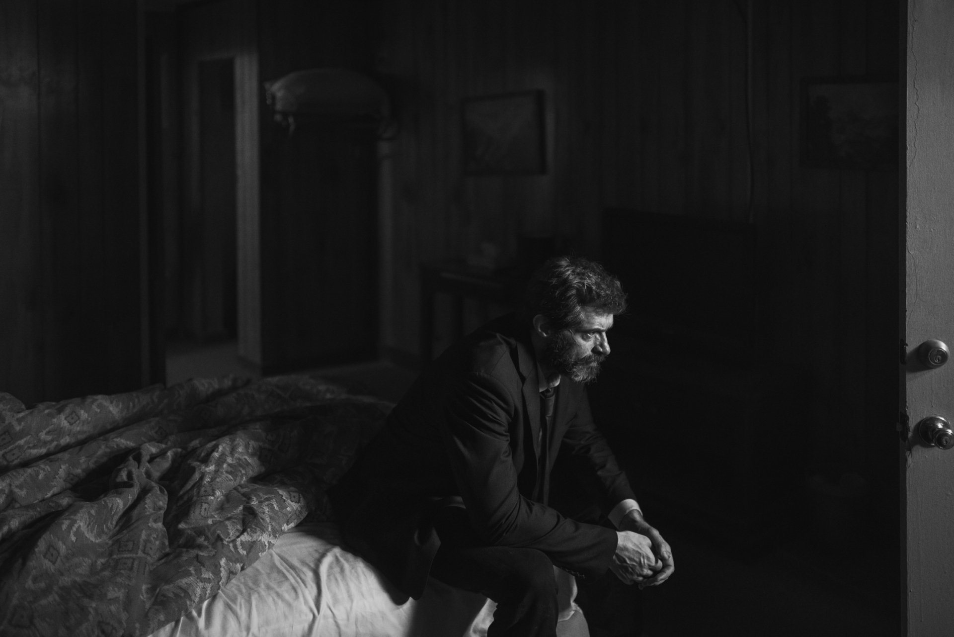 Black and white HD desktop wallpaper featuring Wolverine from the Logan movie, showing a contemplative moment in a dimly lit room.
