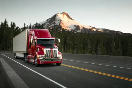 A red Western Star truck driving on a highway with a forest and snow-capped mountain in the background, captured in a crisp 4K Ultra HD desktop wallpaper.