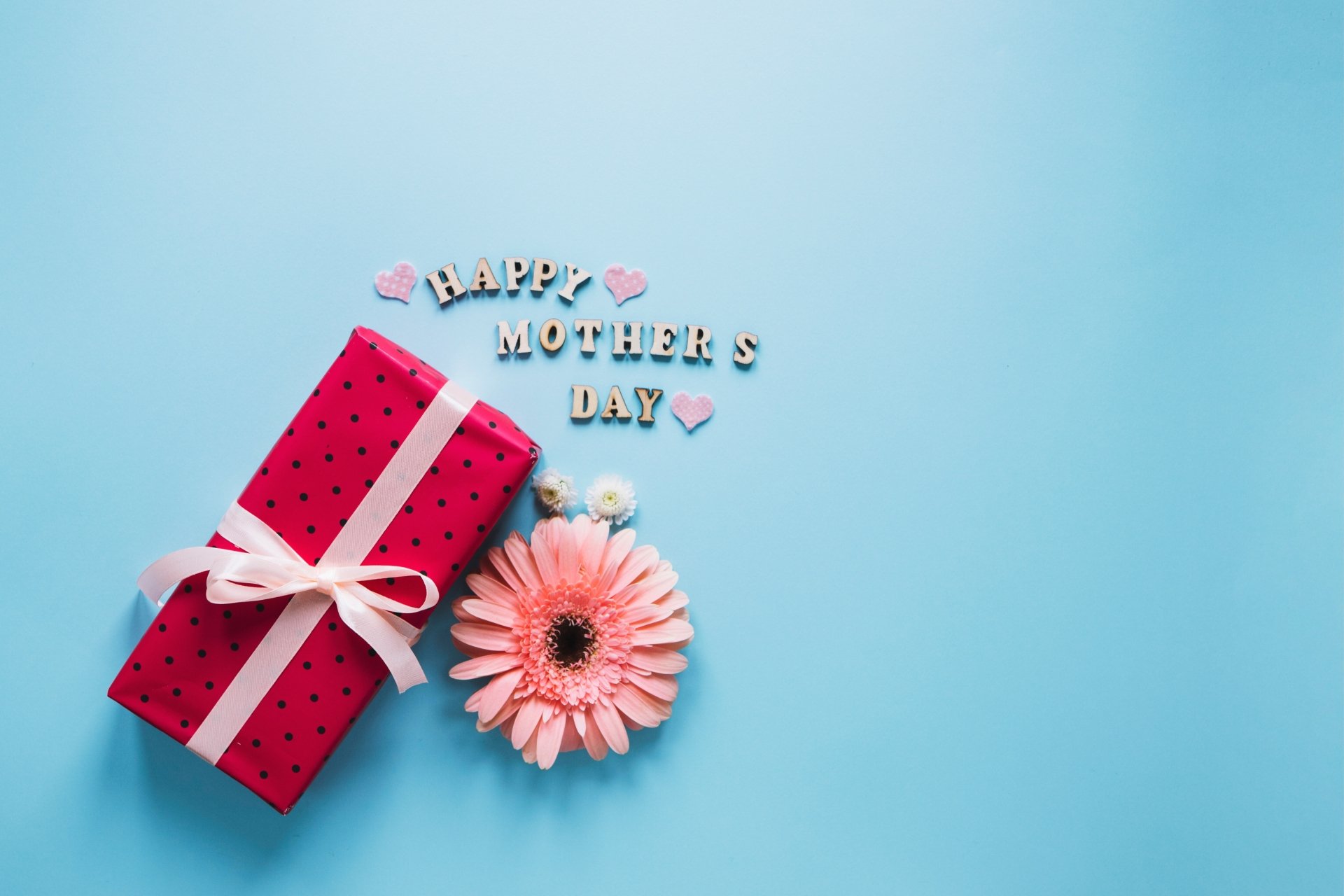 4K Ultra HD desktop wallpaper featuring a pink gift box tied with a ribbon, a single flower, and Happy Mother's Day spelled out on a soft blue background.