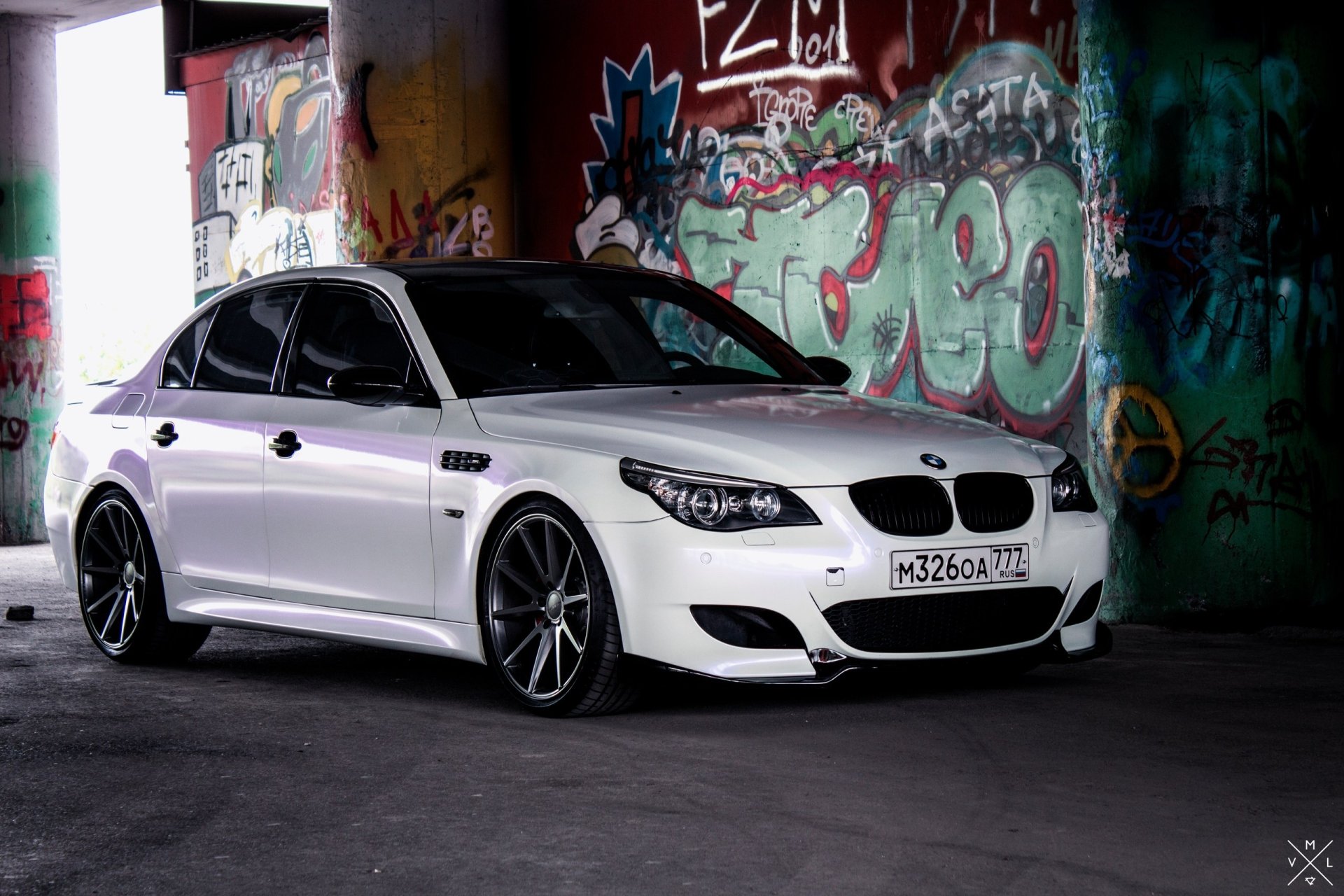 White BMW M5 sedan in a graffiti-covered urban garage, 2K Quad HD car desktop wallpaper background.