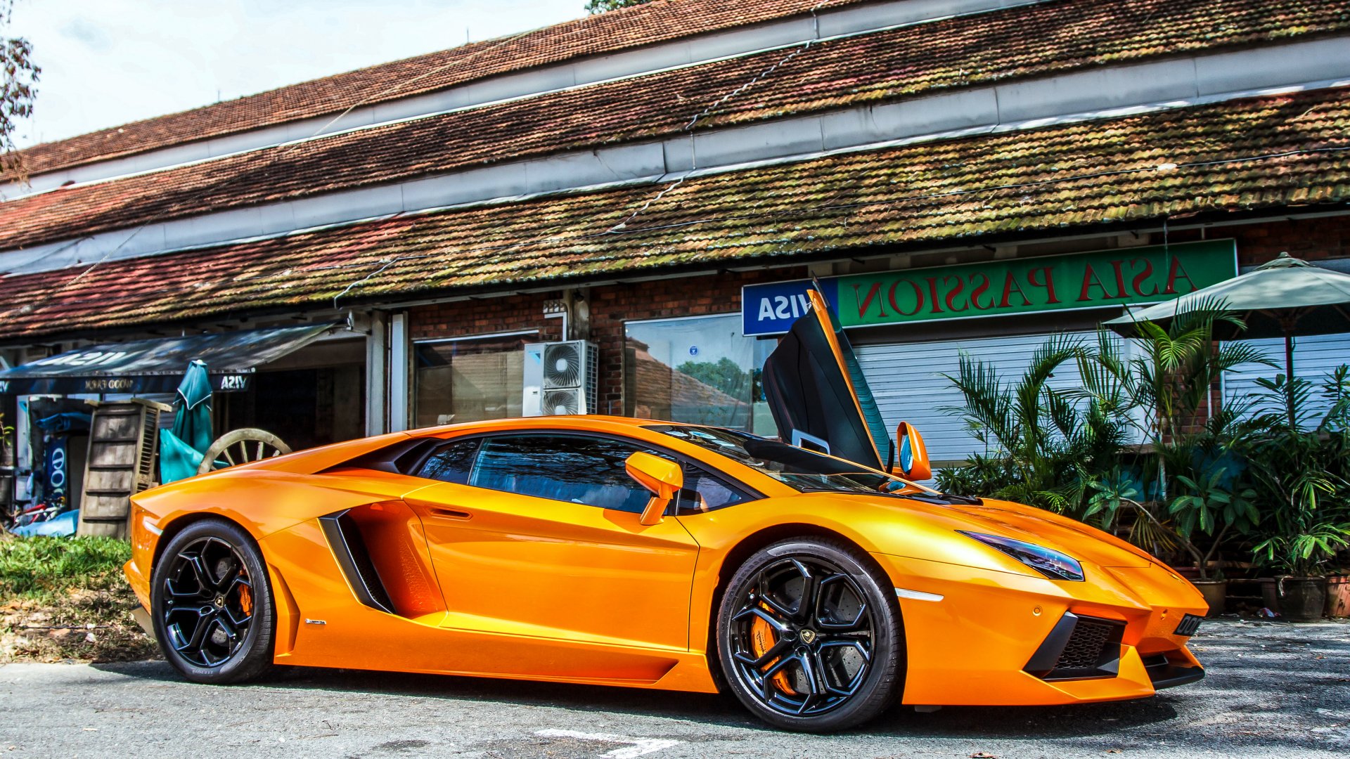Orange Lamborghini Aventador LP 700-4 parked in front of a rustic building, showcased in sharp 4K Ultra HD detail as a PC desktop wallpaper and background.