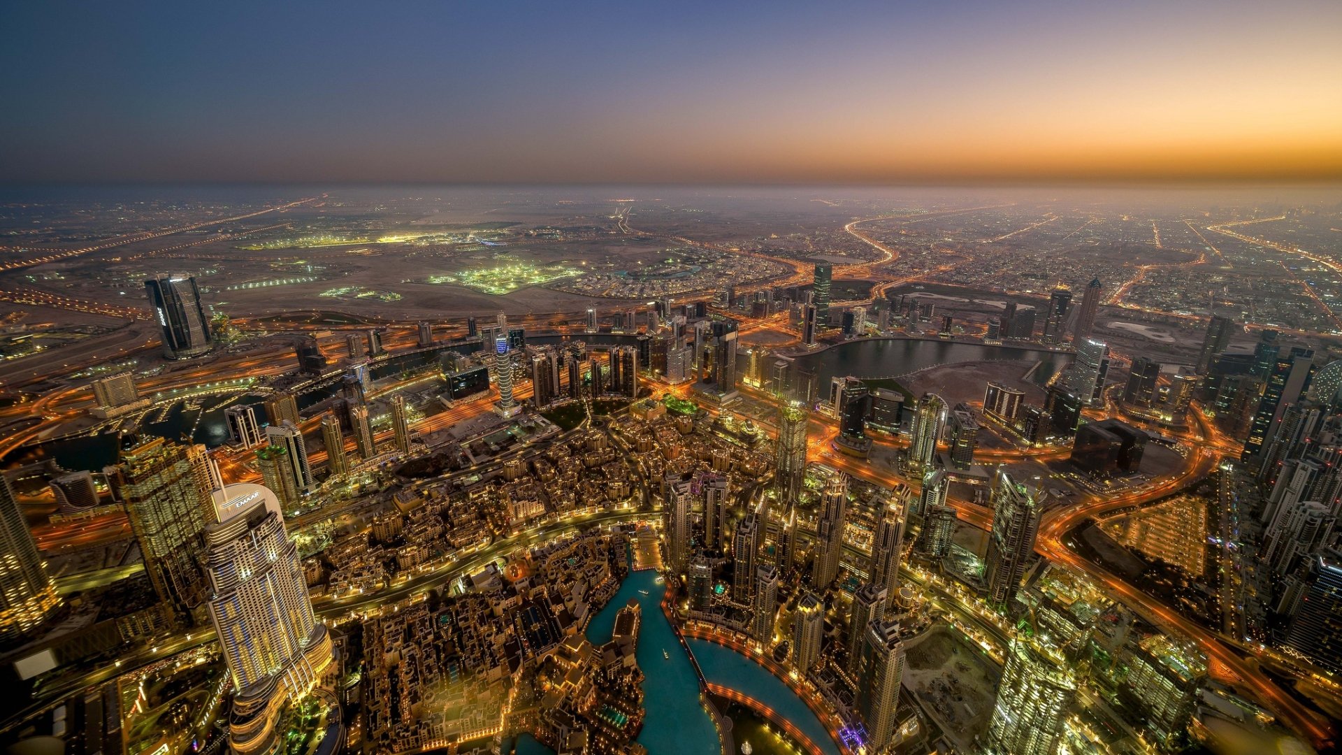A stunning HD desktop wallpaper showcasing Dubai’s vibrant cityscape and skyline at sunset, featuring iconic man-made buildings against a glowing horizon.