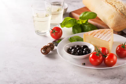 A 4K Ultra HD still life desktop wallpaper featuring cheese, olives, tomatoes, fresh bread, and basil on a white plate with glasses of water on a light surface.