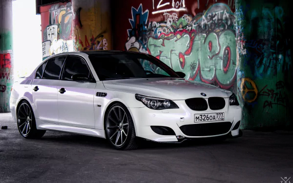 White BMW M5 sedan in a graffiti-covered urban garage, 2K Quad HD car desktop wallpaper background.