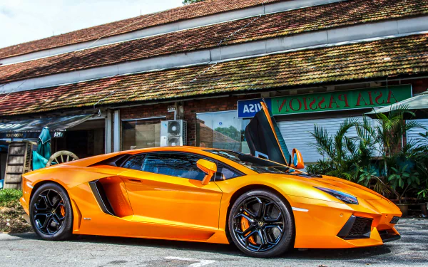 Orange Lamborghini Aventador LP 700-4 parked in front of a rustic building, showcased in sharp 4K Ultra HD detail as a PC desktop wallpaper and background.