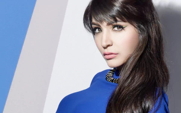 HD desktop wallpaper: close-up of a brown-eyed Indian woman with long black hair, wearing a bold necklace and a blue top against a pale backdrop.