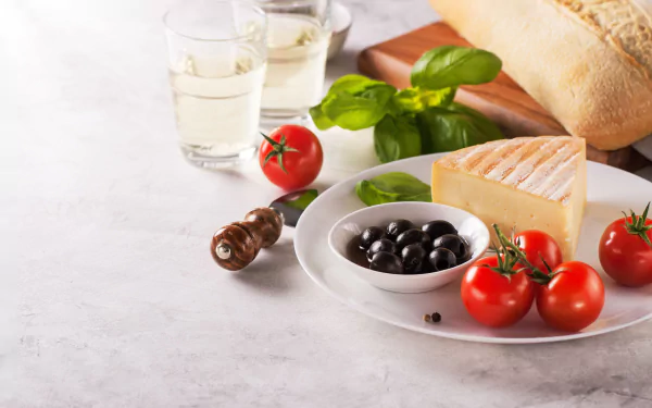 A 4K Ultra HD still life desktop wallpaper featuring cheese, olives, tomatoes, fresh bread, and basil on a white plate with glasses of water on a light surface.