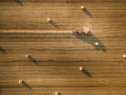 Aerial view of a tractor gathering haystacks in a golden summer field, captured as an HD PC desktop wallpaper and background.