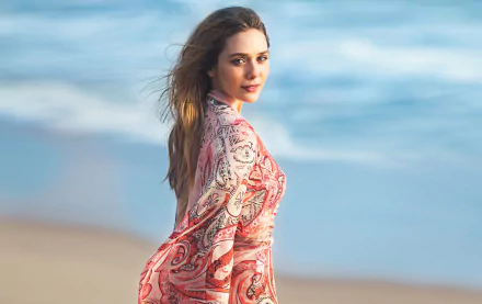 HD desktop wallpaper featuring celebrity Elizabeth Olsen standing on a beach with a calm ocean background and wearing a patterned, flowing dress.