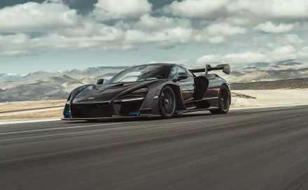 A sleek black McLaren Senna supercar speeding on a racetrack under a cloudy sky, captured in high-definition for a dynamic PC desktop wallpaper.