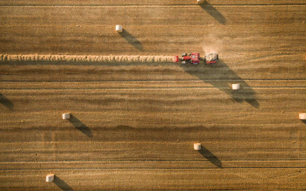 Aerial view of a tractor gathering haystacks in a golden summer field, captured as an HD PC desktop wallpaper and background.