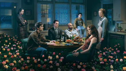 HD PC desktop wallpaper of a scene from the TV show Six Feet Under: family gathered around a dim dining table amid scattered roses and moody blue-green light.