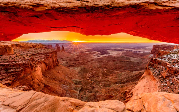 Sunrise view through Mesa Arch over vast desert landscape, captured in vibrant colors for a stunning 4K Ultra HD nature desktop wallpaper.