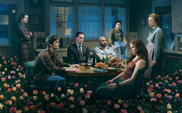 HD PC desktop wallpaper of a scene from the TV show Six Feet Under: family gathered around a dim dining table amid scattered roses and moody blue-green light.