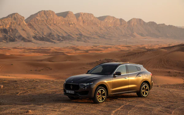 A silver Maserati Levante SUV parked in a vast desert with rugged mountains in the background, captured in stunning 4K Ultra HD.
