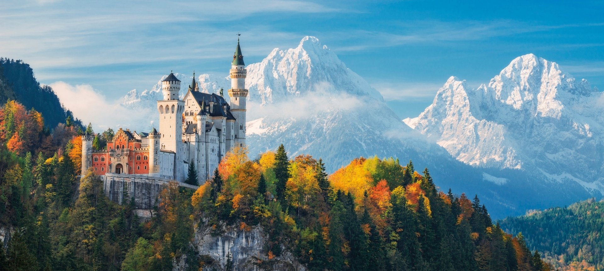 Neuschwanstein Castle stands majestically against a backdrop of mountains in Germany, surrounded by vibrant autumn foliage, showcasing stunning architecture and natural beauty.