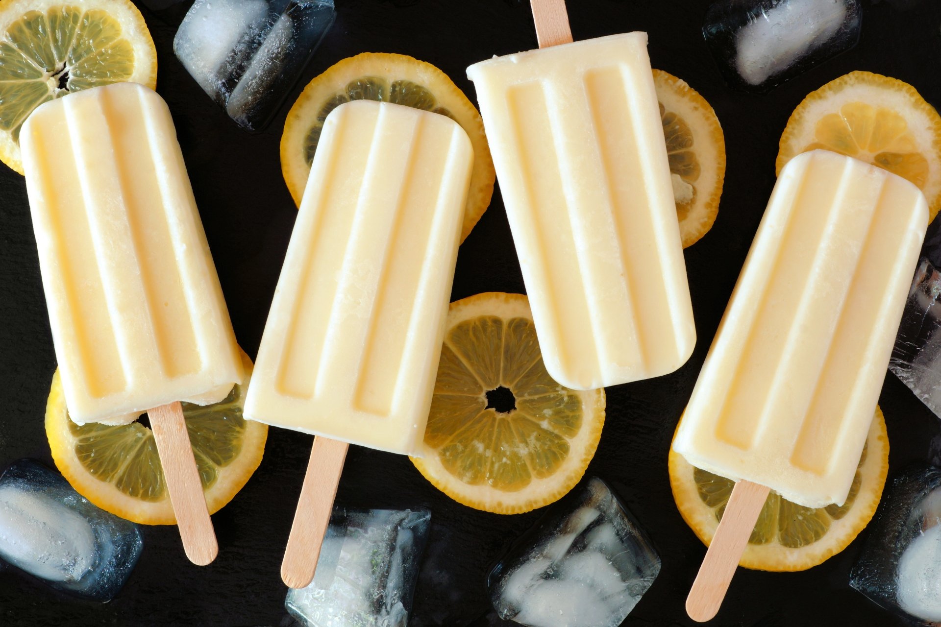 4K Ultra HD wallpaper featuring creamy popsicles with lemon slices and ice cubes on a dark background, highlighting refreshing ice cream treats.
