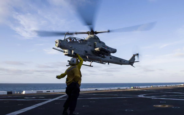Bell AH-1 Cobra attack helicopter hovering over an aircraft carrier deck with a deck crew member, military aircraft in HD desktop wallpaper